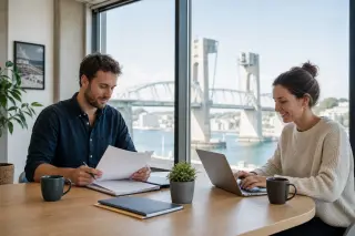 Two entrepreneurs working in a bright coworking space in Brest with sea view and Pont de Recouvrance visible, embodying the city's business-friendly and maritime atmosphere.