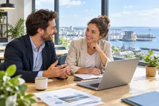 Deux jeunes entrepreneurs discutent autour d'une table dans un espace de coworking lumineux, avec vue sur le littoral finistérien à travers une grande fenêtre, ambiance professionnelle et détendue.